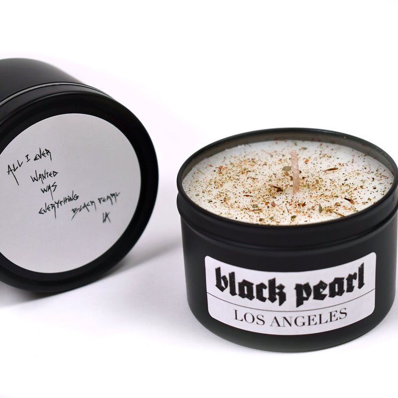 two candles, one with lid on and lid says all I ever wanted was everything by black pearl la and the other is lid off with white wax and floral spread on top